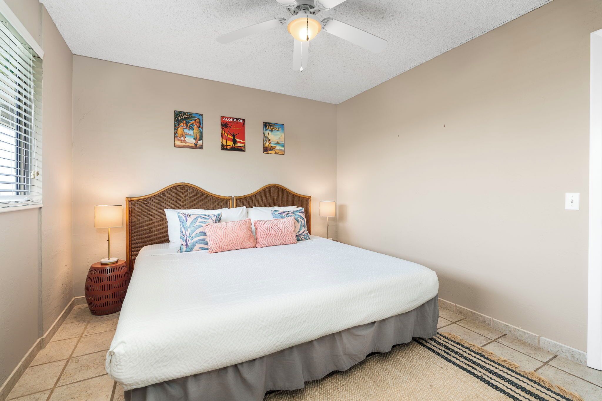 A bedroom with a large bed, two bedside lamps, a ceiling fan, and three wall posters.