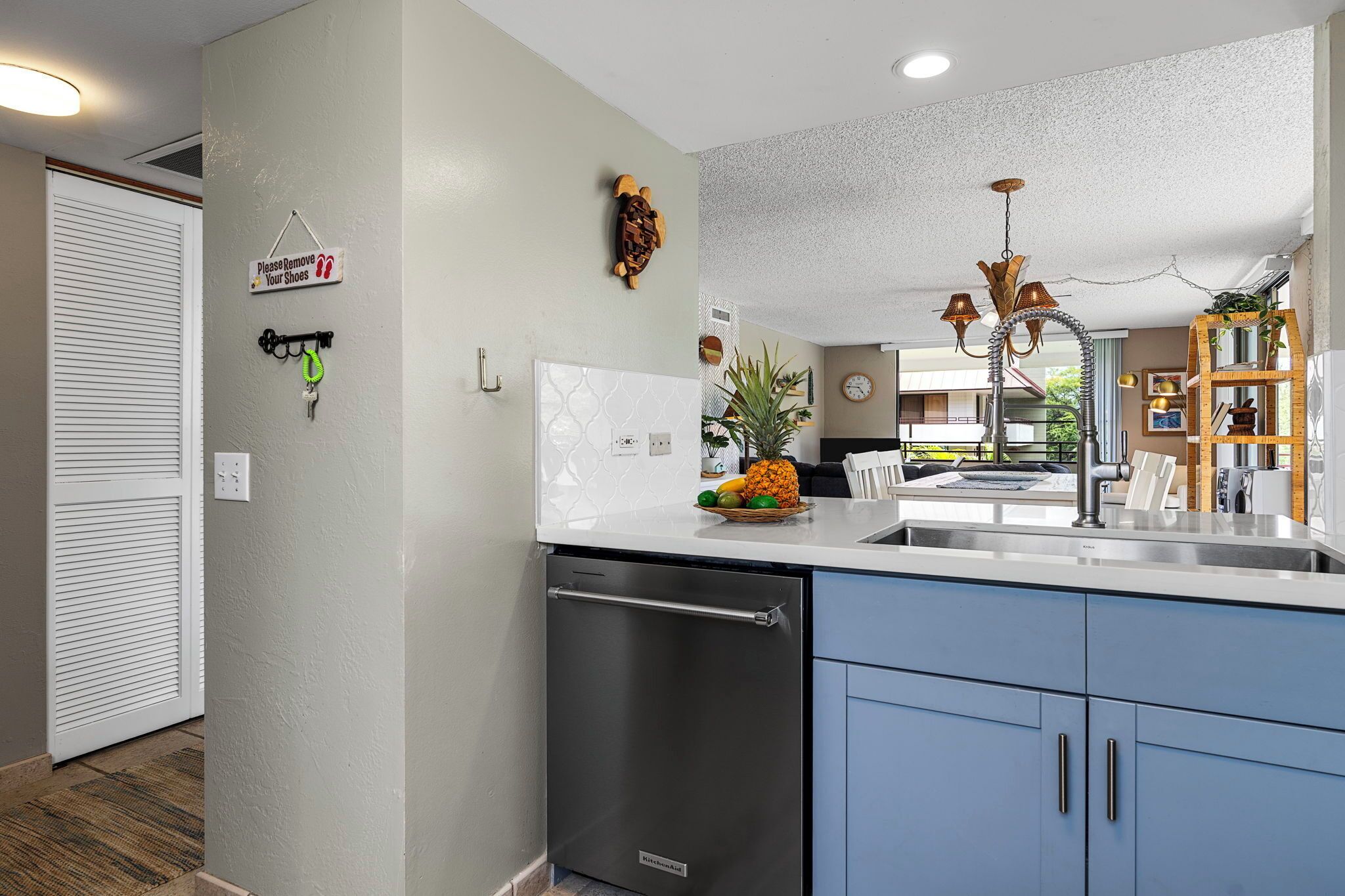 A kitchen with a dishwasher, a fruit bowl on the counter, and a sign on the wall.