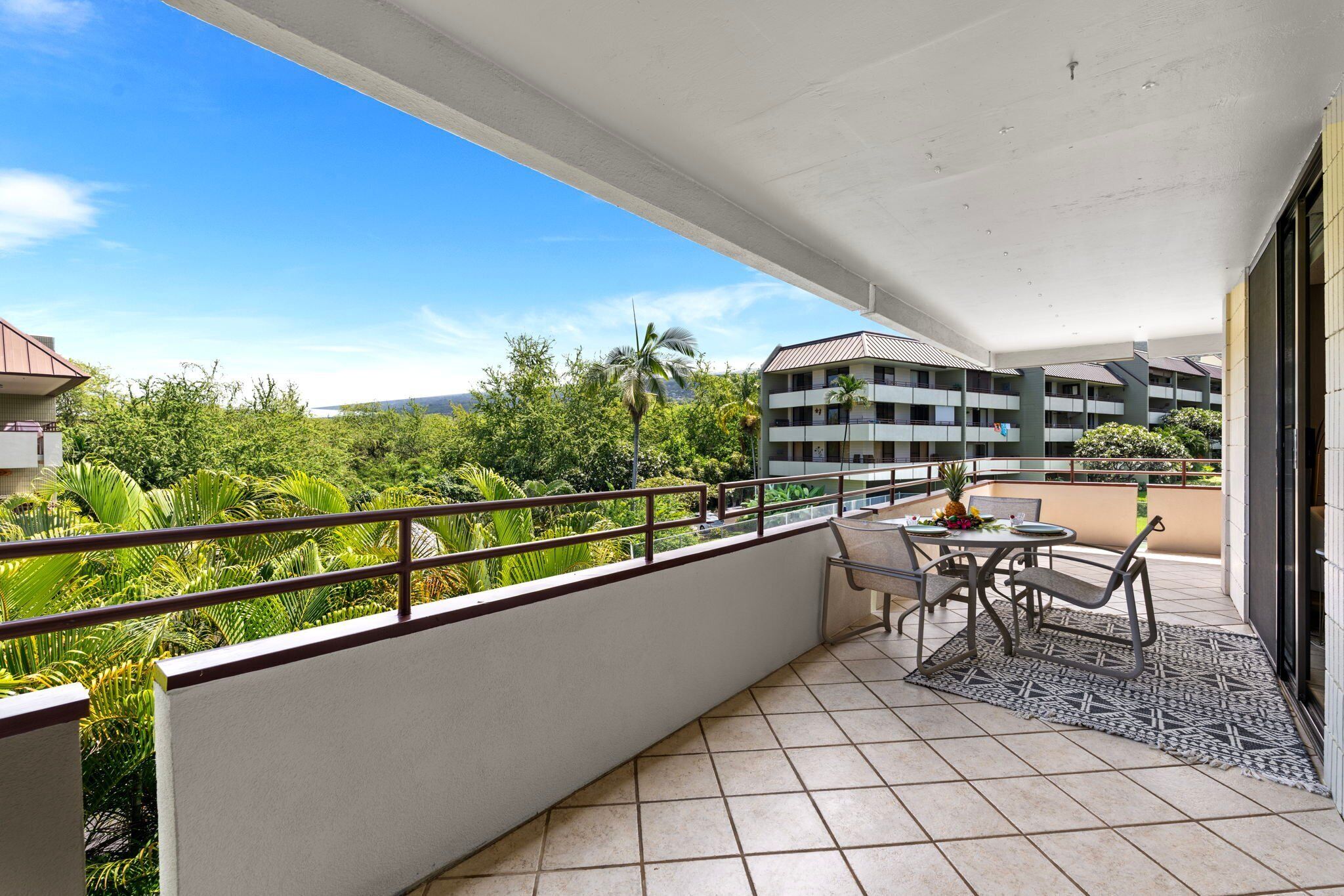 A balcony with a tiled floor, a table with chairs, and a view of greenery and buildings.