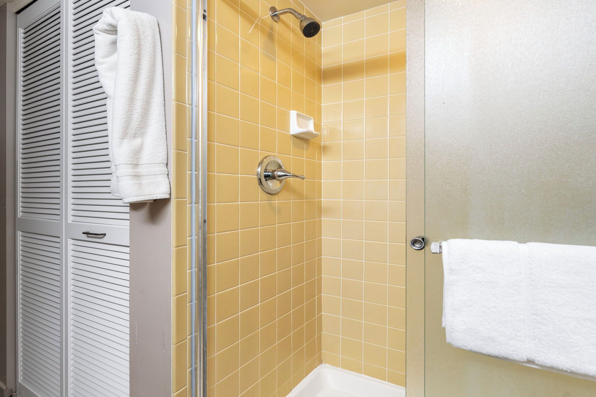 Een badkamer met gele betegelde muren, een wit bad en een douchecabine van glas.