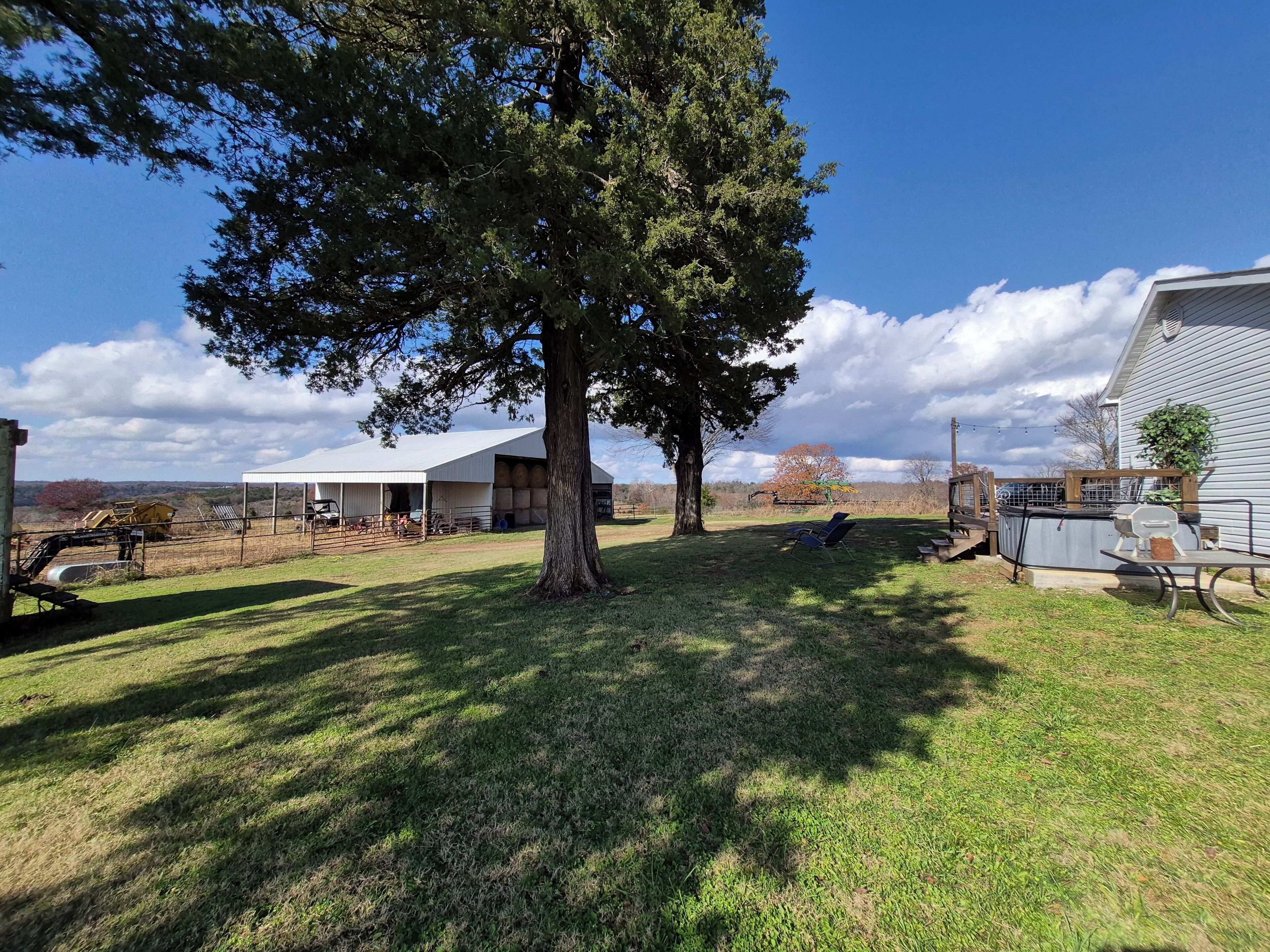 A spacious backyard with a large tree, a covered outdoor area, and a fenced-in section with farm equipment.