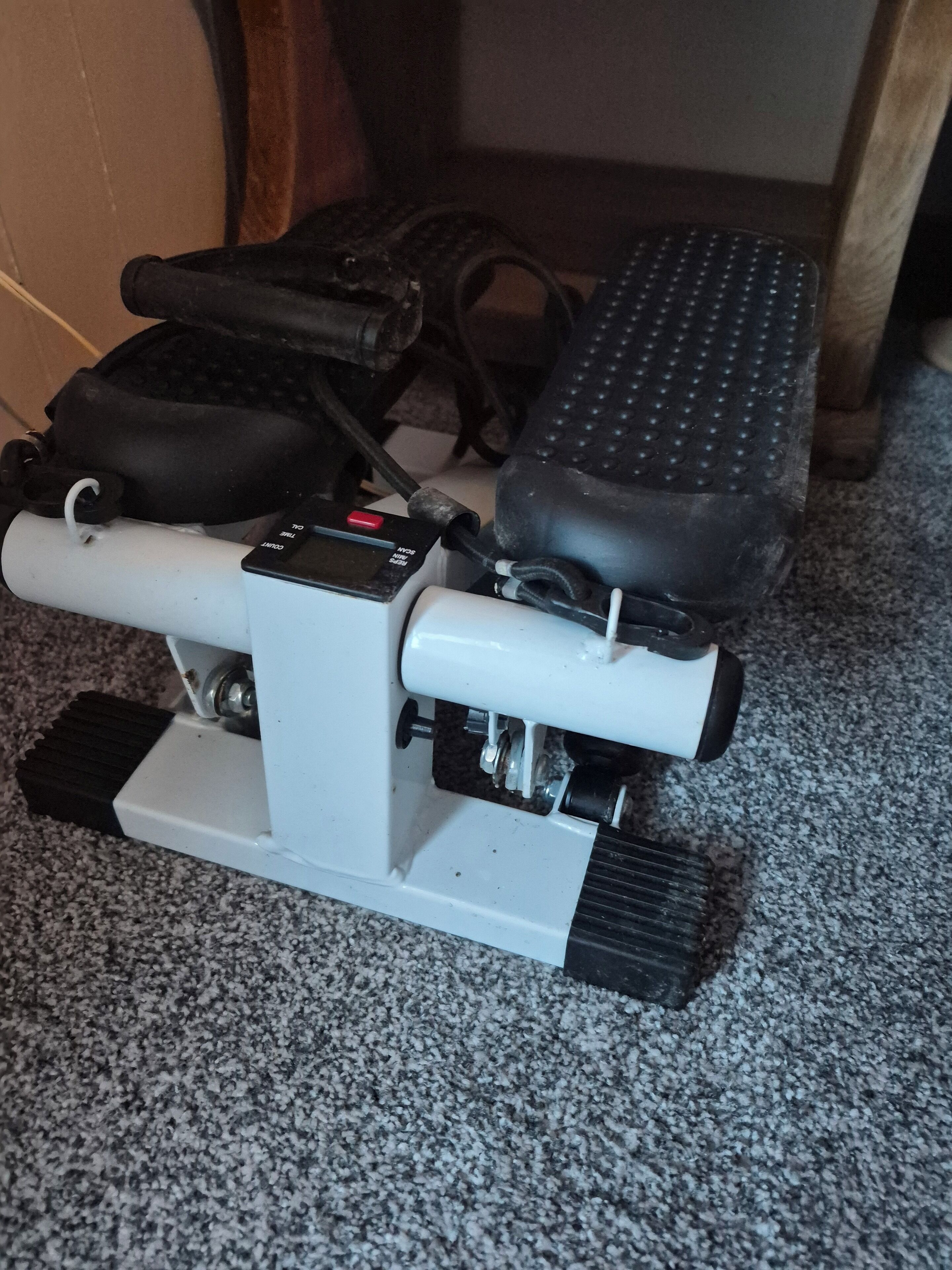 A white mechanical device with black foot pedals and a control panel on a carpeted floor.