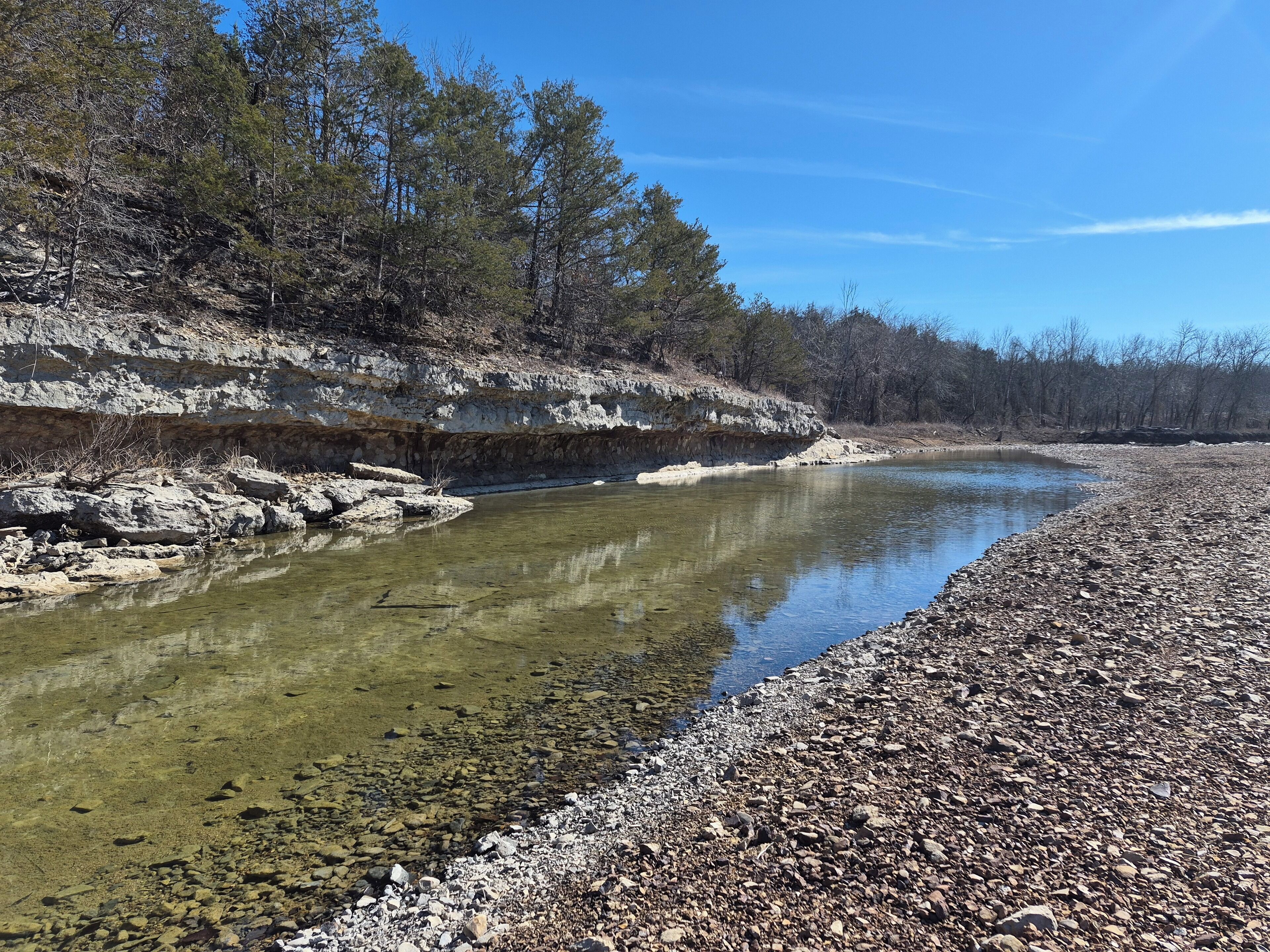 A river with clear water, surrounded by rocky terrain and trees.