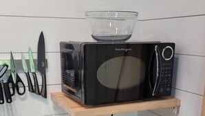 Una cocina con un microondas sobre un estante de madera, una cafetera y varios cuchillos en la pared.