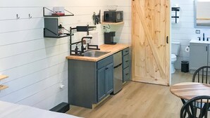 Cocina compacta con armarios de madera, un lavamanos y un microondas. Hay una puerta corrediza que da a un baño.