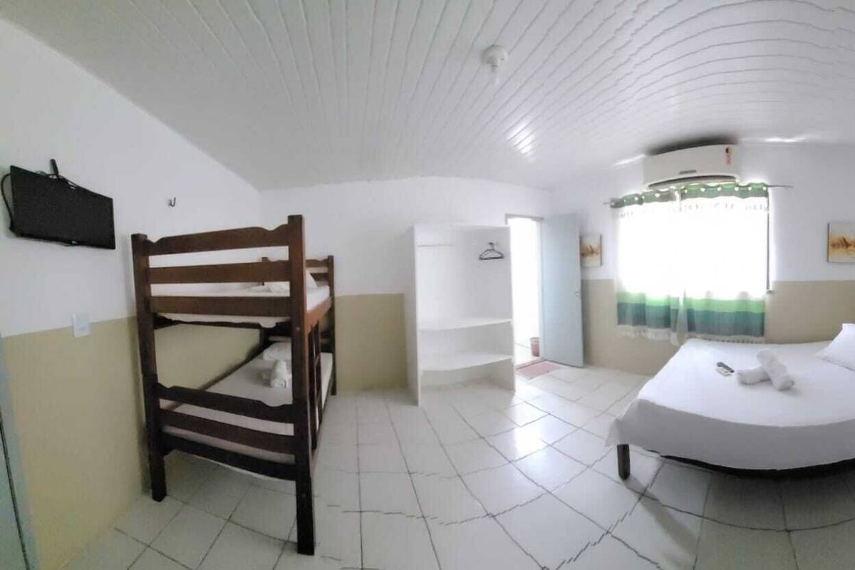 Une chambre avec un lit superposé, un lit simple, un téléviseur fixé au mur, une fenêtre avec des rideaux et un ventilateur de plafond.