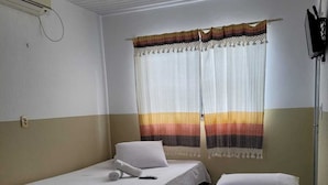 A hotel room with two single beds, a window with a striped curtain, a ceiling fan, and a wall-mounted TV. - Sol do Centro Pousada (Fortaleza)