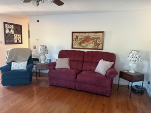A living room with a red sofa, blue armchair, and a coffee table. - Peaceful 1-bedroom cottage surrounded by apple orchards in charming Flat Rock (Flat Rock)