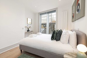 Ein modernes Schlafzimmer mit einem großen Bett, Blick auf den Balkon und einer minimalistischen Einrichtung.