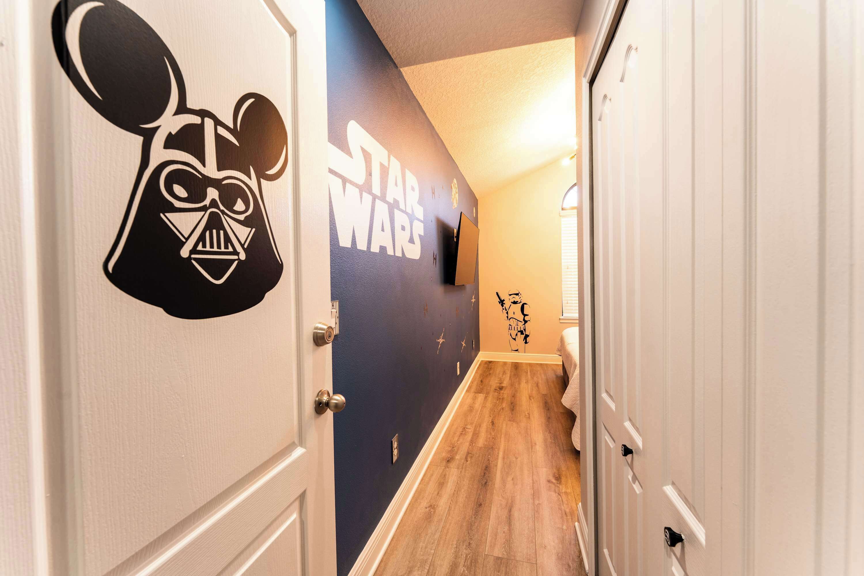 A hallway with Star Wars-themed wall decals, wooden flooring, and white doors.