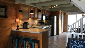A cozy kitchen with wooden cabinets, a central island with bar stools, a refrigerator, and a microwave. - Beachwalk 20, Steps to the Beach, Outdoor Pool (Ocean City)