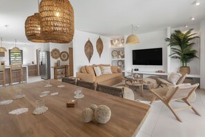 A modern living room with a wooden dining table, a sofa, and a TV. - Villa Kaia (oyster pond)
