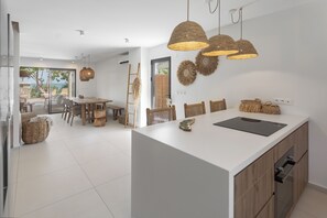 A modern kitchen with a large island, wooden chairs, and woven light fixtures. - Villa Kaia (oyster pond)