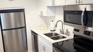 A modern kitchen with stainless steel appliances, white cabinetry, and a clock on the wall. - Tropical Isle 209🌴Beach Access👙 (Fort Walton Beach)