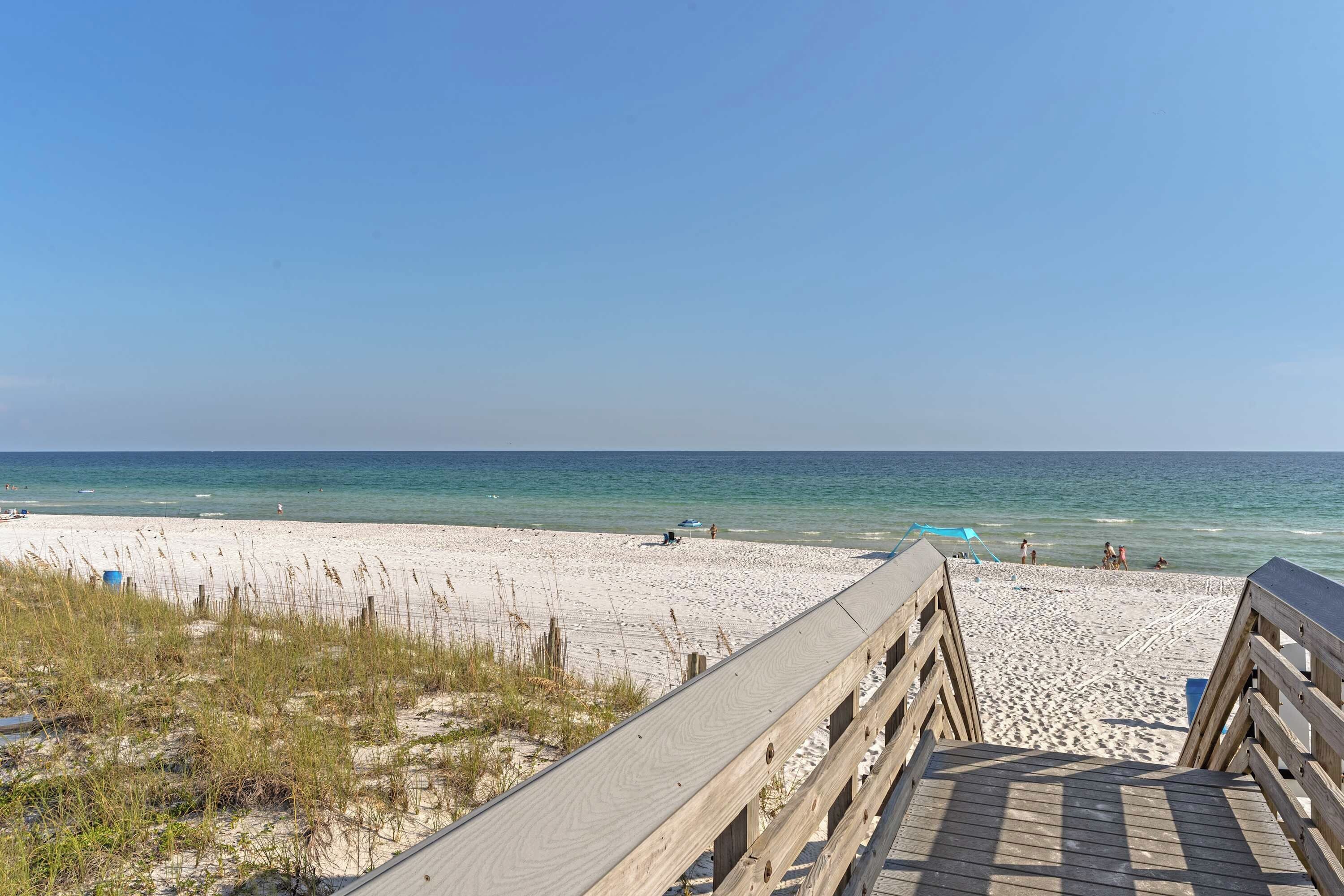 A wooden boardwalk leading to a sandy beach with clear blue water.
