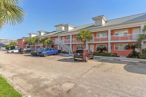 A multi-story motel with a red facade, white balconies, and a parking area with several vehicles. - Tropical Isle 209🌴Beach Access👙 (Fort Walton Beach)