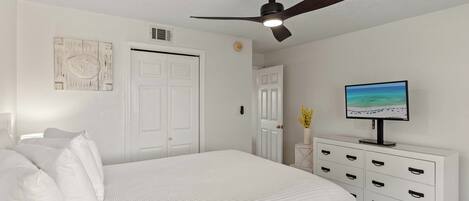 A bedroom with a bed, a ceiling fan, a white dresser, a television, and a wall-mounted artwork.