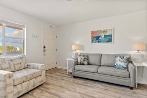 A living room with a grey sofa, a patterned armchair, and a painting on the wall. - Tropical Isle 209🌴Beach Access👙 (Fort Walton Beach)