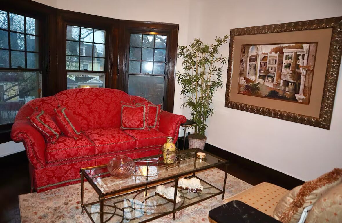 Ein rotes Sofa mit floralem Muster, ein Glastisch, ein Blumentopf und ein gerahmtes Bild an der Wand.