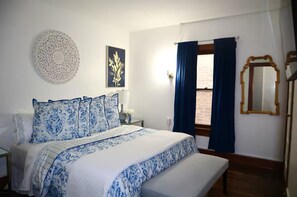 Een slaapkamer met een bed, een nachtkastje, een spiegel aan de muur en een raam met gordijnen.