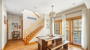 A spacious living area with a wooden staircase, a dining table with benches, and large windows with blinds. - Pine Haven Retreat | Walk to Downtown & Pool (Sisters)
