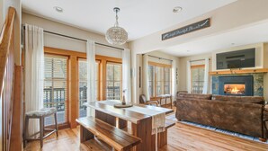 A spacious living room with a wooden floor, a fireplace, a sofa, and a dining area with a bench and table. - Pine Haven Retreat | Walk to Downtown & Pool (Sisters)
