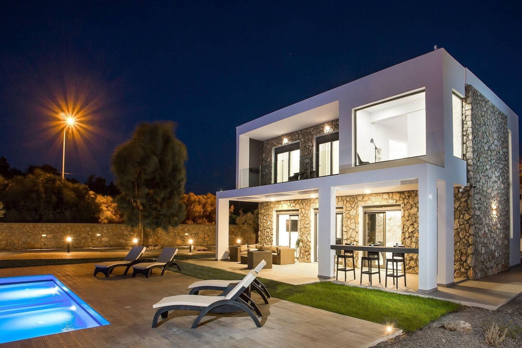 Una casa moderna de dos pisos con piscina, mobiliario exterior y paredes de piedra.
