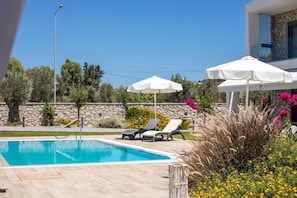A swimming pool with lounge chairs and umbrellas, surrounded by stone walls and vegetation. - Luxurious Villa with Private Pool for 8 (Kalythies)