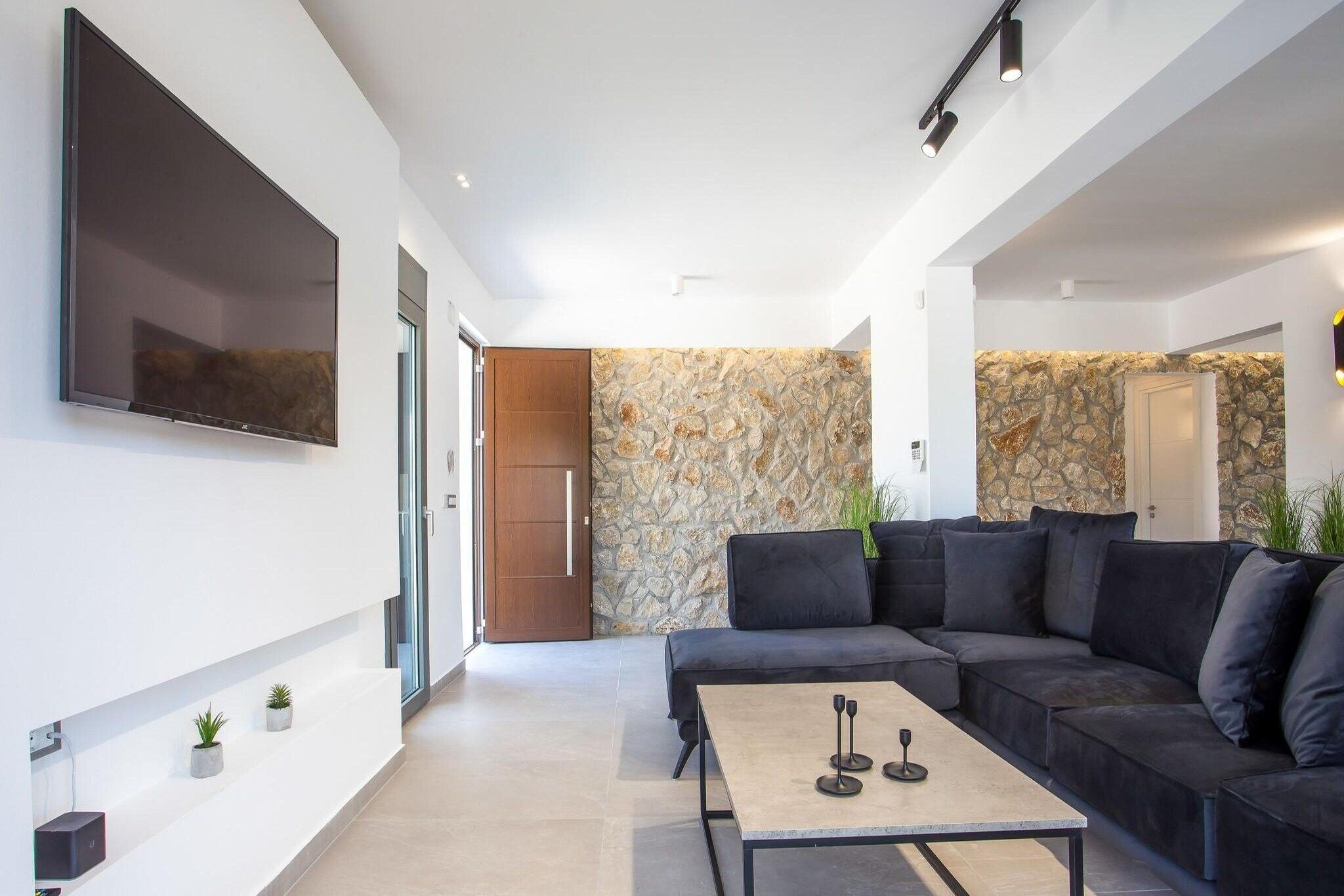 Una sala moderna con un televisor de pantalla plana grande, un sofá de color oscuro, una mesa de centro y una pared decorativa de piedra.