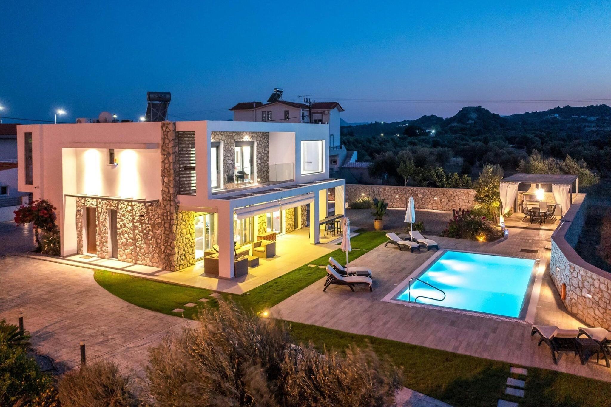 A modern two-story house with a swimming pool, outdoor seating, and a stone facade.