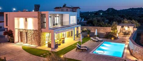 A modern two-story house with a swimming pool, outdoor seating, and a stone facade.