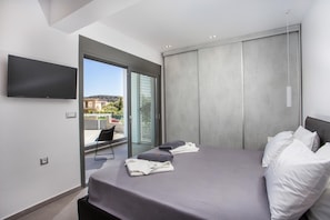A modern bedroom with a bed, a chair, a TV, and a view of the outside. - Luxurious Villa with Private Pool for 8 (Kalythies)