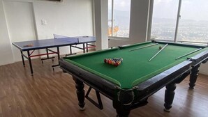 A pool table with balls, a ping pong table, and a view of a city through large windows.