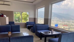 A modern lounge area with blue upholstered seating, a coffee table, and large windows offering a view of a cityscape and mountains.