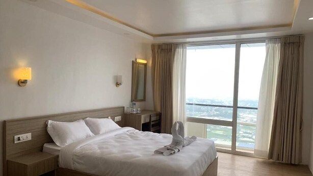 A hotel room with a large bed, a nightstand, a bedside table, a mirror, and a view of the city through large windows.