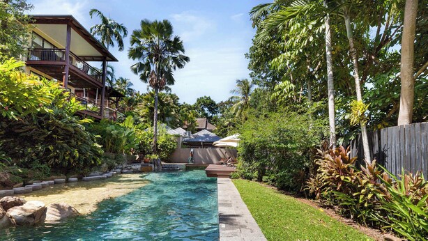 A pool area with clear water, surrounded by lush greenery and a wooden fence. - Vistas @ The Point Su (Port Douglas)