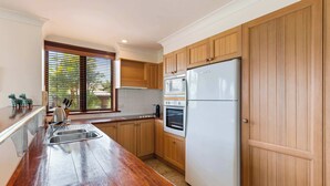 A kitchen with wooden cabinets, a stainless steel sink, a refrigerator, and an oven. - Vistas @ The Point Su (Port Douglas)