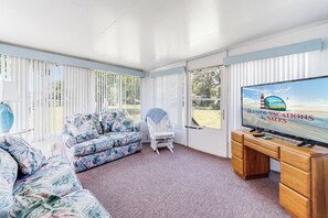 Ein Zimmer mit Fernseher, einer Couch, einem Sessel und einem Schreibtisch.