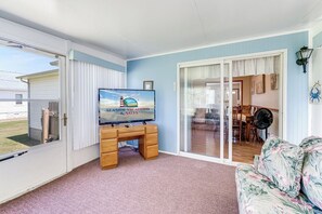 Ein Zimmer mit Fernseher auf Holzständer, einer Couch und einer Schiebetür zu einem Essbereich.