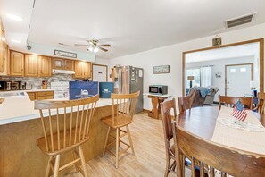 A modern kitchen with wooden cabinets, a dining area with a table and chairs, and a ceiling fan. - Bradford House by Seaside Vacations & Sales (Chincoteague)