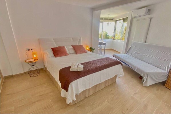 A modern bedroom with a large bed, a sofa, and a small table with a lamp. - Apartment with Sea Views in Mijas Costa (Malaga)