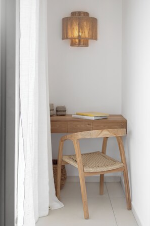 Een houten bureau met een geweven stoel, een lamp en een boek erop.