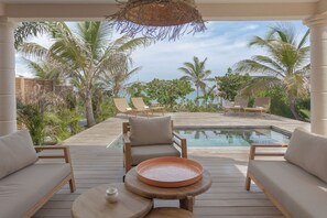 Ein Poolbereich mit Liegestühlen, einem Tisch mit einer Schale und Blick aufs Meer.