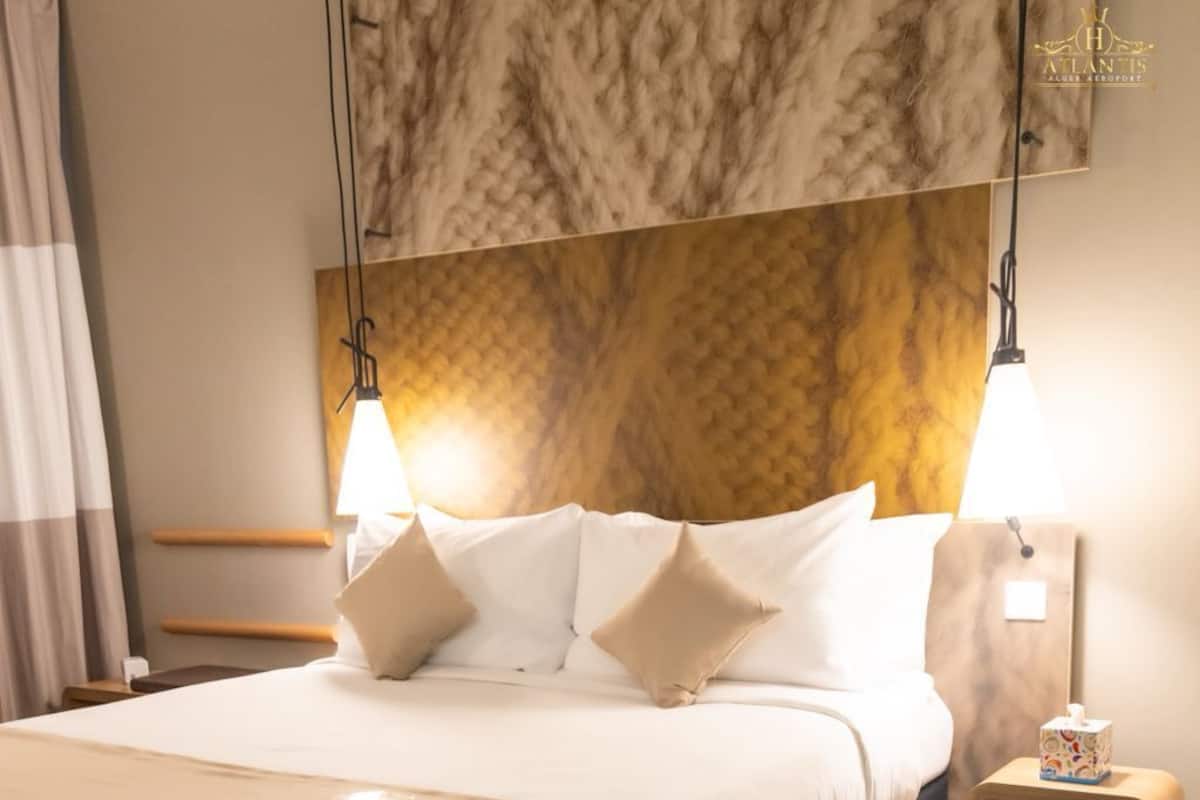Ein Hotelzimmer mit einem großen Bett, zwei Nachttischen, einem Bettkopfteil mit strukturierter Gestaltung und einer Wandleuchte.