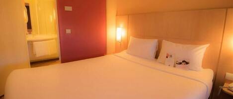 Una habitación de hotel con una cama grande, una mesita de noche y un velador.