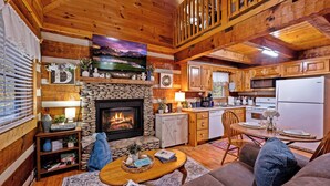 A cozy cabin interior with a stone fireplace, wooden ceiling, a dining area, and a kitchen with wooden cabinets. - Hot Tub, View, Pool Table, Fireplace, Honeymoon! (Sevierville)