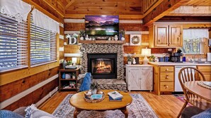 A cozy cabin interior with a stone fireplace, wooden walls, a dining area, and a kitchen. - Hot Tub, View, Pool Table, Fireplace, Honeymoon! (Sevierville)