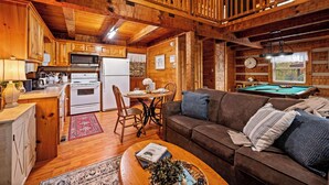 A cozy cabin interior with a wooden dining area, a pool table, and a living room with a couch and coffee table. - Hot Tub, View, Pool Table, Fireplace, Honeymoon! (Sevierville)