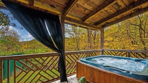 A wooden deck with a hot tub, a wooden railing, and a view of autumn trees. - Hot Tub, View, Pool Table, Fireplace, Honeymoon! (Sevierville)