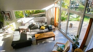 A modern living room with a sofa, coffee table, and large windows offering a view of the outdoors. - Atypical house in a green setting only 20 minutes from Nice (Contes)